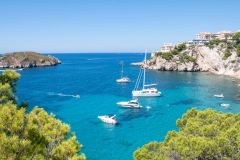 The lights of a sun. Sailing boat on the sea, rocks and blue sky.